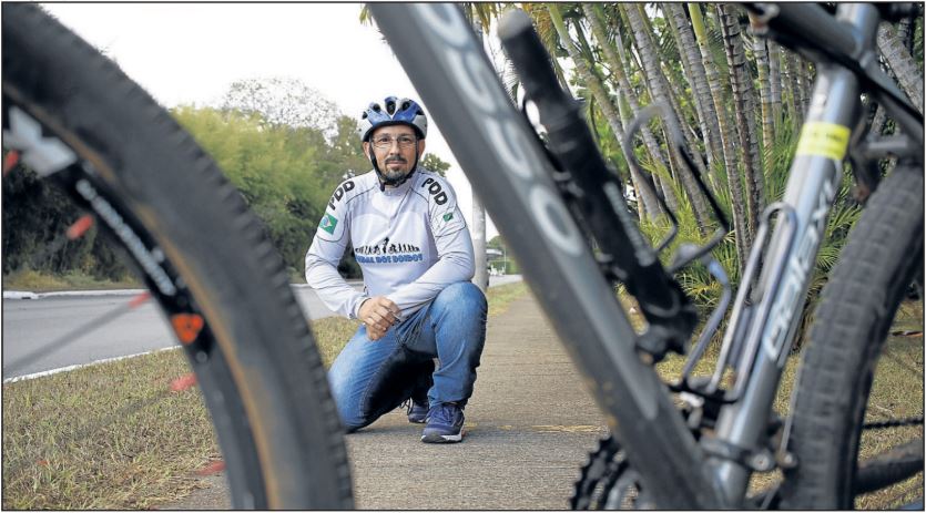 Imagem mostra, Marco Antônio, agachado por trás da bicicleta, através do quadro da mesma.